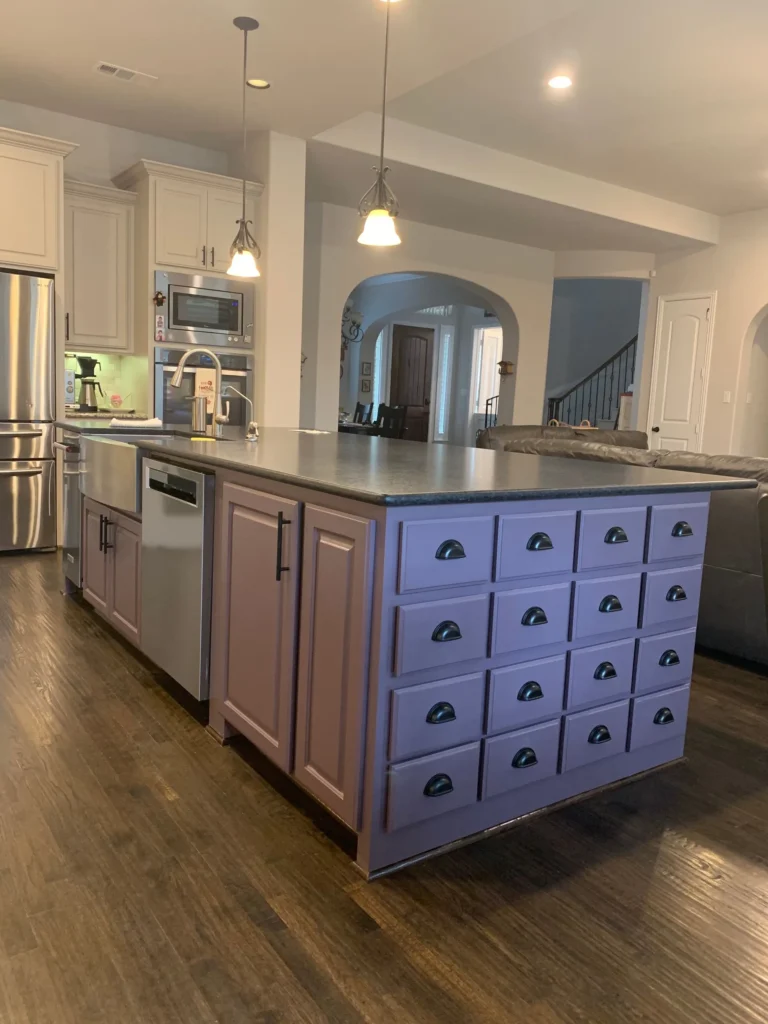 Kitchen island with custom cabinetry featuring purple drawers and black handles, stainless steel appliances, and modern lighting, showcasing home remodeling design by The Perfect Cabinet Company.