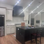 Modern kitchen featuring a custom island with dark cabinetry, stainless steel appliances, and stylish lighting, showcasing The Perfect Cabinet's design expertise.