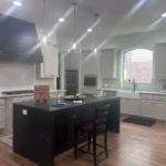 Custom kitchen island with black cabinetry, modern lighting, and wooden flooring, showcasing The Perfect Cabinet's design expertise.