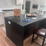 Custom kitchen island featuring dark cabinetry and a countertop, with decorative items and a chair, showcasing The Perfect Cabinet's design offerings.