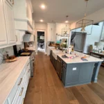 Custom kitchen island with dark cabinetry and white countertops, surrounded by light wood flooring and modern fixtures, showcasing a stylish kitchen design by The Perfect Cabinet.