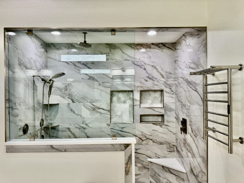 Modern glass shower enclosure with marble tiles, sleek showerhead, built-in shelves, and towel rack, showcasing luxury bathroom design for home remodeling.