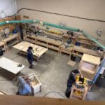 Workshop scene with craftsmen working on custom cabinetry projects, showcasing woodworking tools and equipment in The Perfect Cabinet Shop.