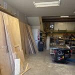 Woodworking shop interior with stacked plywood sheets, machinery, and tools, showcasing the craftsmanship behind custom cabinetry at The Perfect Cabinet Shop.