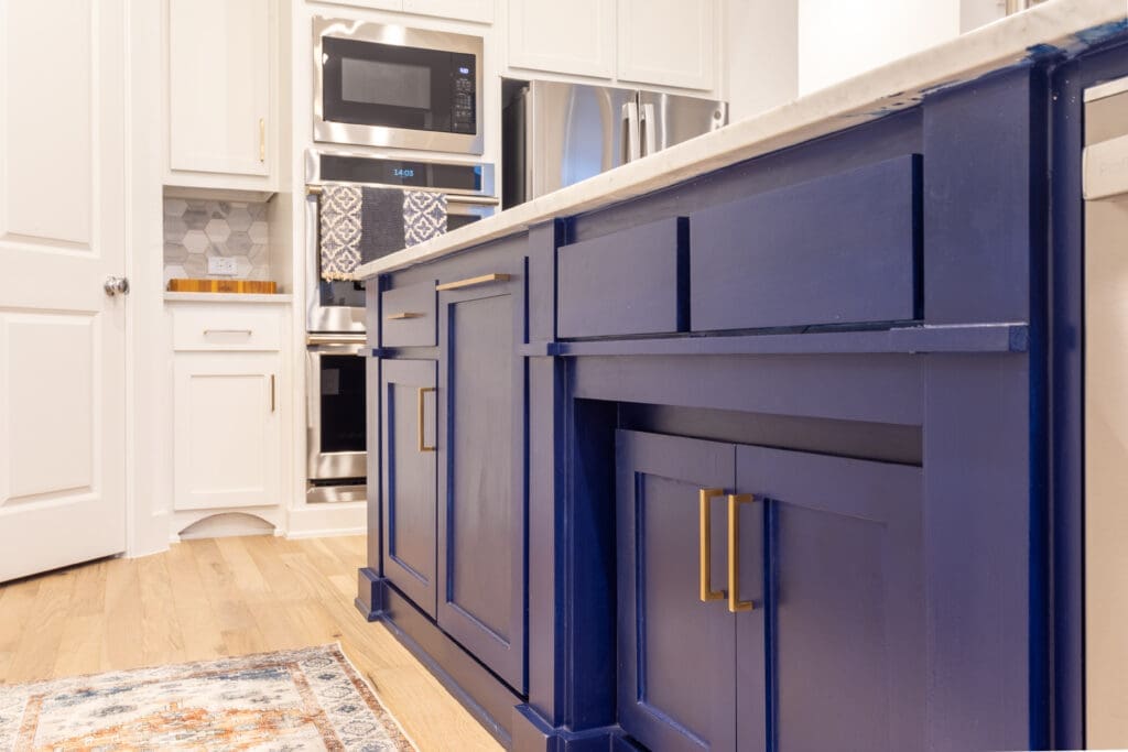Modern kitchen featuring navy blue cabinetry with gold hardware, stainless steel appliances, and a light wood floor, illustrating a stylish kitchen remodel.