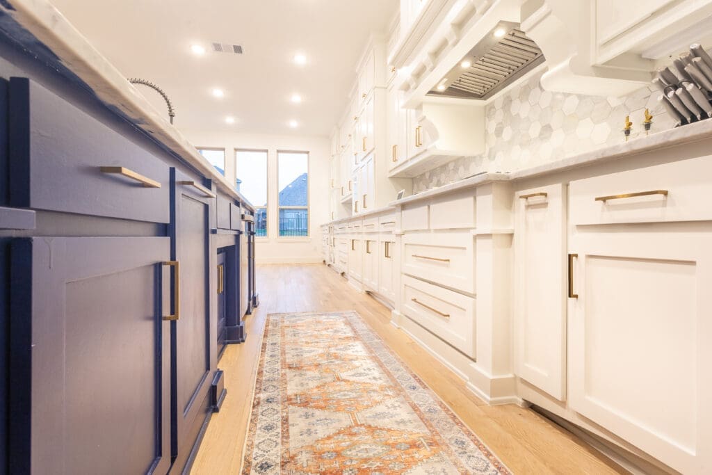 Modern kitchen featuring custom cabinetry in navy blue and white, with a stylish hexagon backsplash, hardwood flooring, and decorative area rug, showcasing the craftsmanship of The Perfect Cabinet Company.
