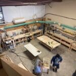 Woodworking shop interior with workbenches, tools, and a craftsman assembling cabinetry projects for The Perfect Cabinet Shop.