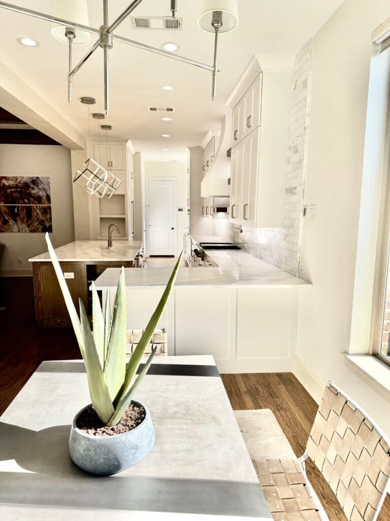 Modern kitchen interior featuring white cabinetry, marble countertops, and a decorative plant centerpiece on a table, showcasing home remodeling design ideas.