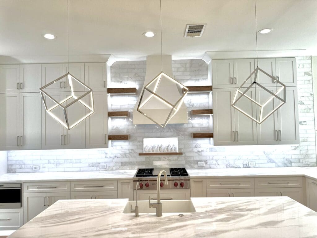Modern kitchen featuring white cabinetry, geometric pendant lights, marble backsplash, and a spacious countertop, highlighting custom cabinetry and remodeling design.