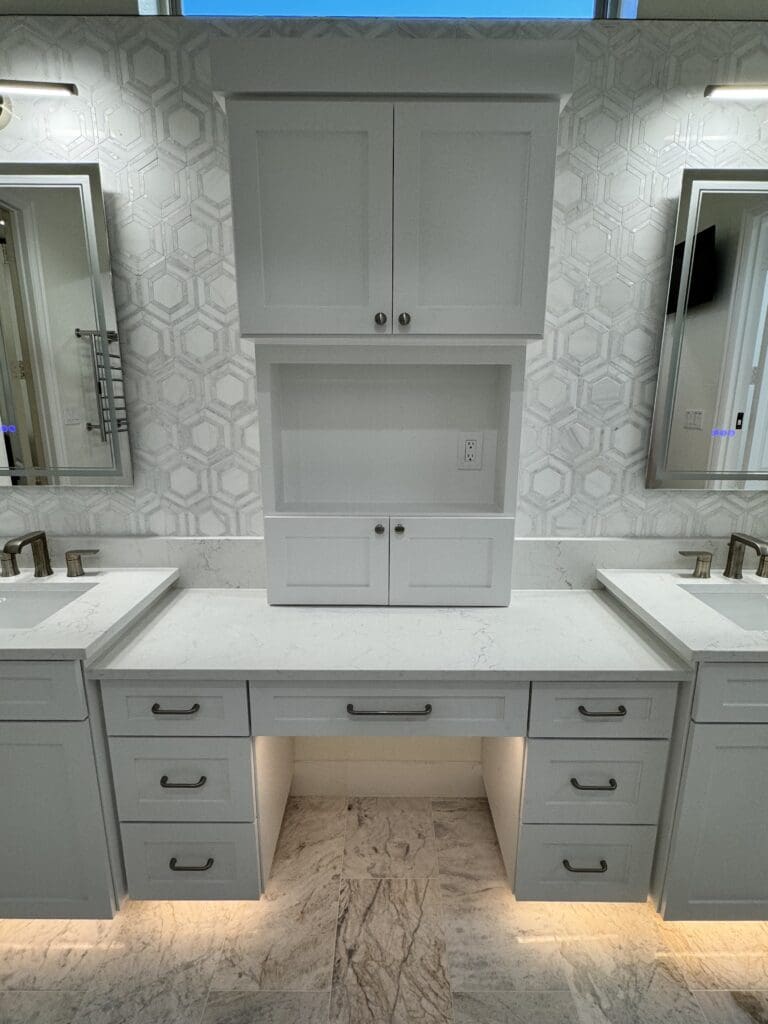 Modern white bathroom vanity with dual sinks, hexagonal tile backsplash, and illuminated cabinetry, showcasing custom cabinetry design by The Perfect Cabinet Company.
