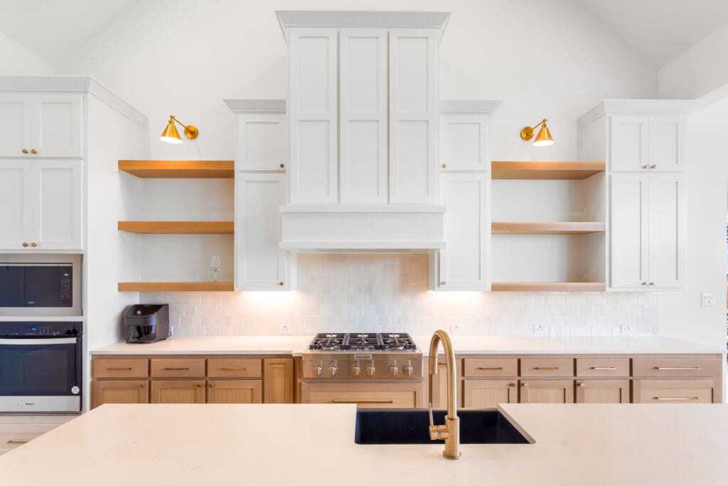 Modern kitchen design featuring custom cabinetry, white upper cabinets, wooden lower cabinets, gold accents, and a gas stove with a sleek countertop and sink, emphasizing quality craftsmanship and renovation inspiration.