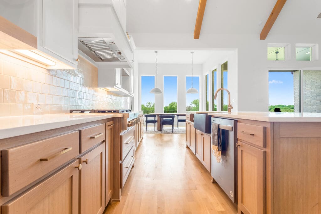 Modern kitchen interior with wooden cabinetry, white countertops, and large windows showcasing outdoor views, highlighting trends in kitchen remodeling for Collin County homes.