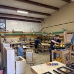 Cabinetry workshop with craftsmen working on custom cabinetry projects, showcasing woodworking tools and materials.