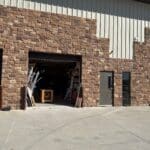 Exterior view of The Perfect Cabinet Shop showcasing a stone and metal building with an open garage entrance and cabinetry materials visible inside.
