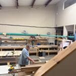 Man working in a cabinetry workshop surrounded by tools and wood materials, showcasing custom cabinetry craftsmanship for The Perfect Cabinet Shop.