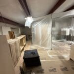 Interior view of a cabinetry workshop featuring unfinished cabinetry pieces, a black storage box, and plastic sheeting indicating an active remodeling project by The Perfect Cabinet Shop.