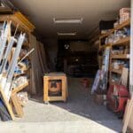 Woodworking shop interior with shelves of materials, tools, and a workbench, showcasing the craftsmanship environment of The Perfect Cabinet Shop.