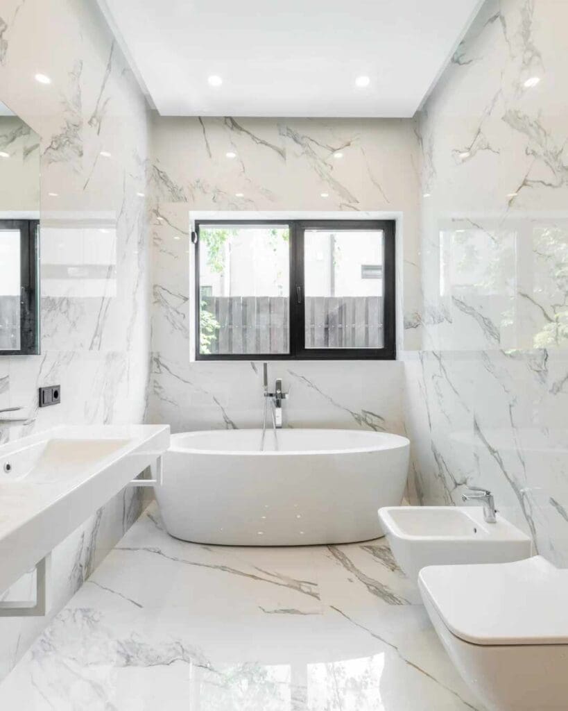Modern bathroom featuring a freestanding white bathtub, sleek vanity with a mirror, and elegant marble walls, showcasing contemporary design ideal for home remodeling inspiration.
