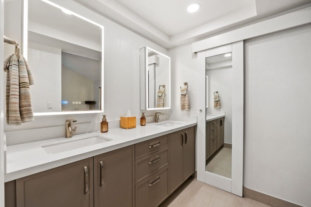 Modern bathroom with dual sinks, illuminated mirrors, stylish cabinetry, and neutral color palette, showcasing custom cabinetry and home remodeling elements.