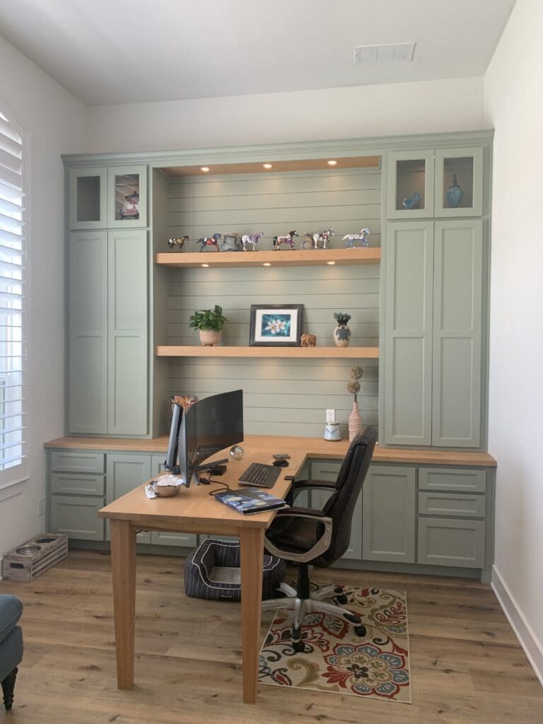 Custom home office featuring green cabinetry, a wooden desk, and decorative shelves with figurines, designed for functional and aesthetic appeal in home remodeling.