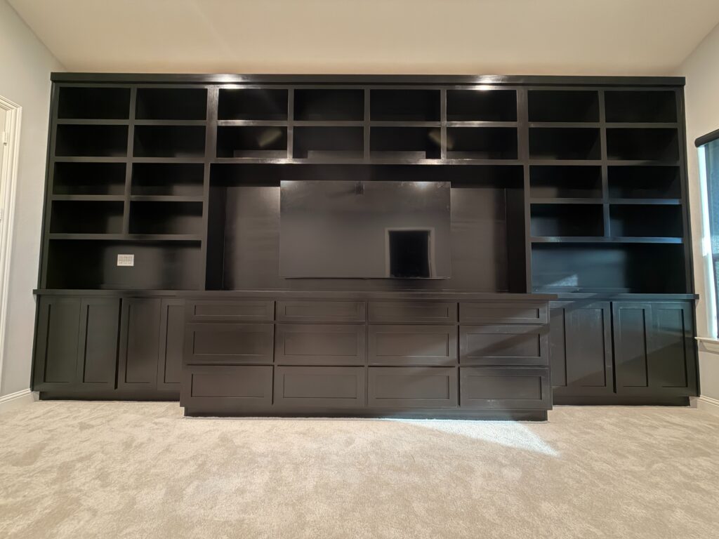 Custom black cabinetry with open shelving and a central space for a television, enhancing home organization and functionality in a modern living area.