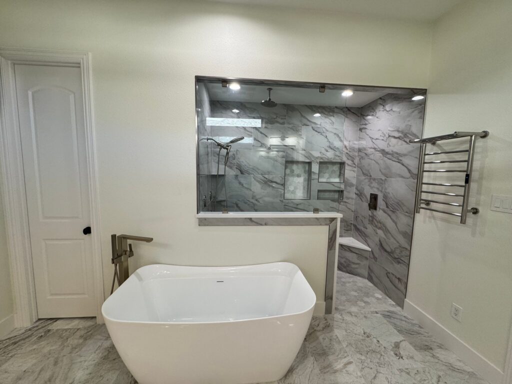 Modern bathroom with freestanding white bathtub, marble tile walls, and glass shower enclosure, showcasing luxury design elements for home remodeling in Collin County and DFW.