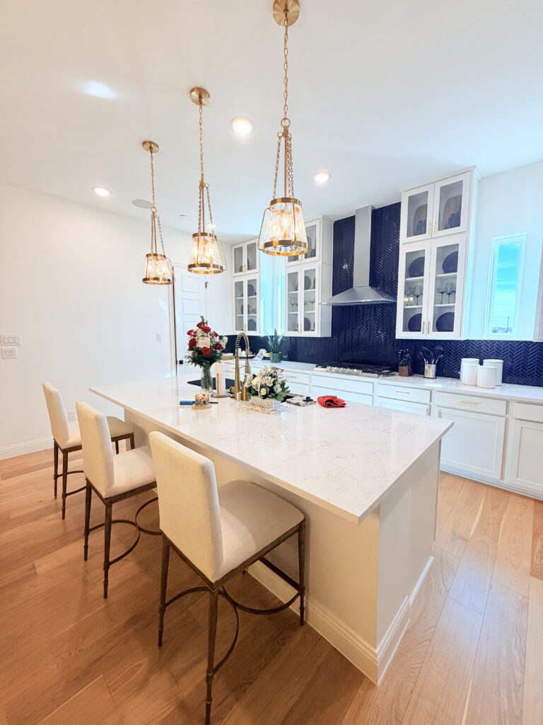 Modern kitchen with a large island, elegant pendant lighting, white cabinetry, and navy backsplash, showcasing a stylish and functional space ideal for remodeling in Collin County and DFW.
