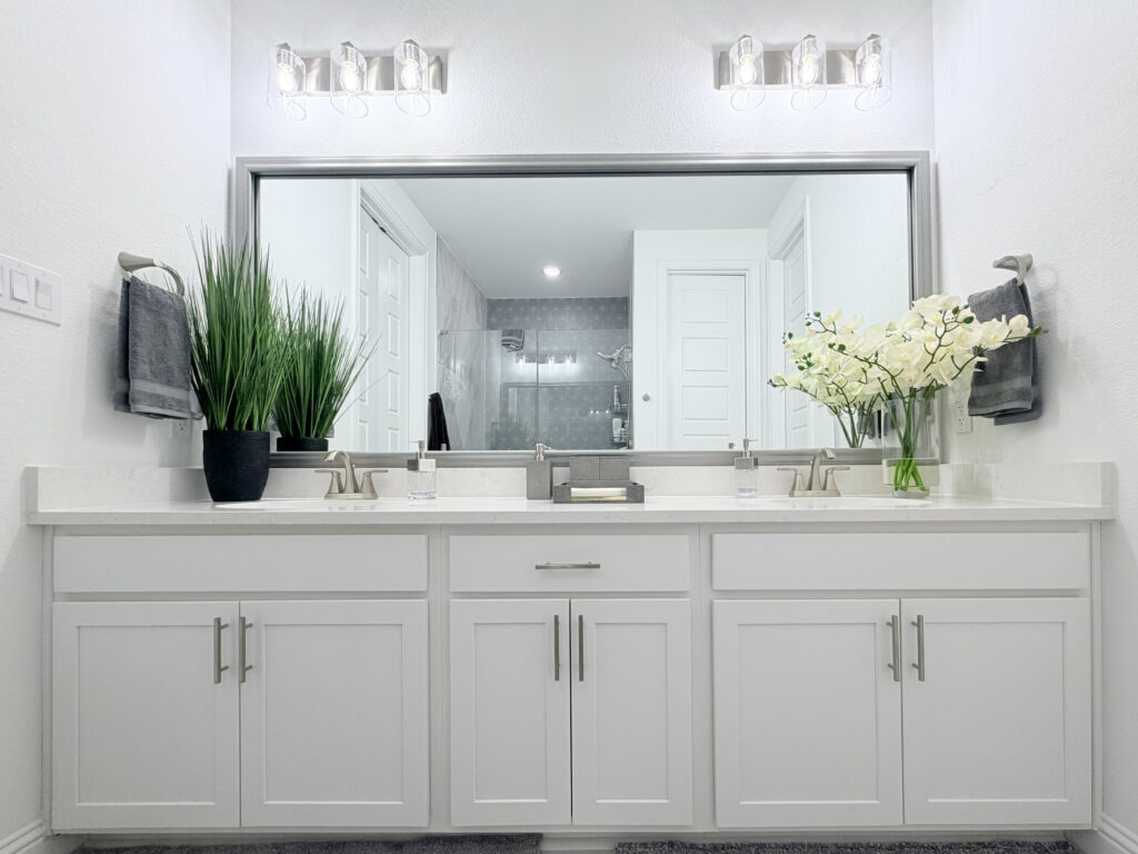 Modern bathroom vanity with white cabinetry, quartz countertop, decorative plants, and elegant lighting, showcasing luxury design elements for home remodeling in Collin County and DFW.