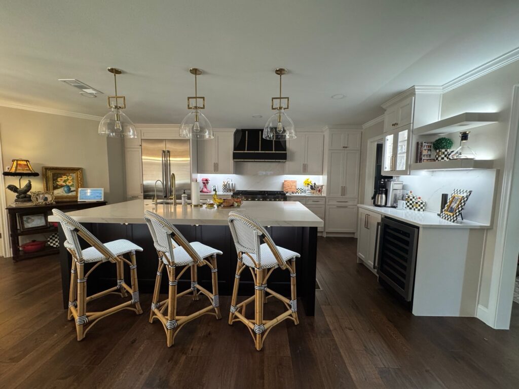 Modern kitchen featuring a large island with seating, stylish pendant lighting, white cabinetry, stainless steel appliances, and a wine storage cabinet, reflecting contemporary design ideal for homeowners in Collin County and DFW.