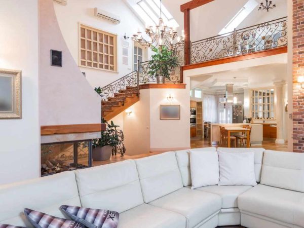 Elegant living room interior featuring a white sectional sofa, decorative pillows, and a warm ambiance with natural light, highlighting a staircase and open kitchen area, ideal for home remodeling inspiration.