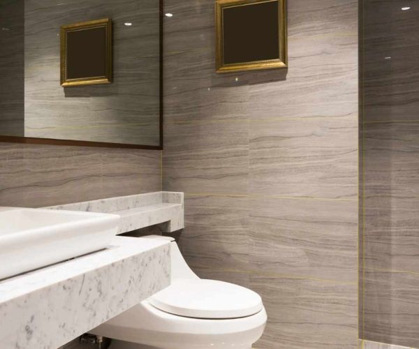 Modern bathroom featuring a sleek marble countertop, elegant toilet, and stylish wall tiles with subtle textures, complemented by framed mirrors and ambient lighting.