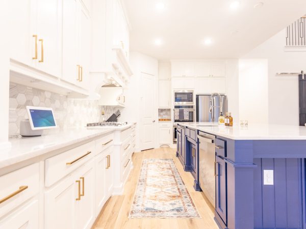 Modern kitchen featuring custom white cabinets with gold handles, a blue island, quartz countertops, and stylish backsplash, emphasizing organization and aesthetic appeal for a functional space.
