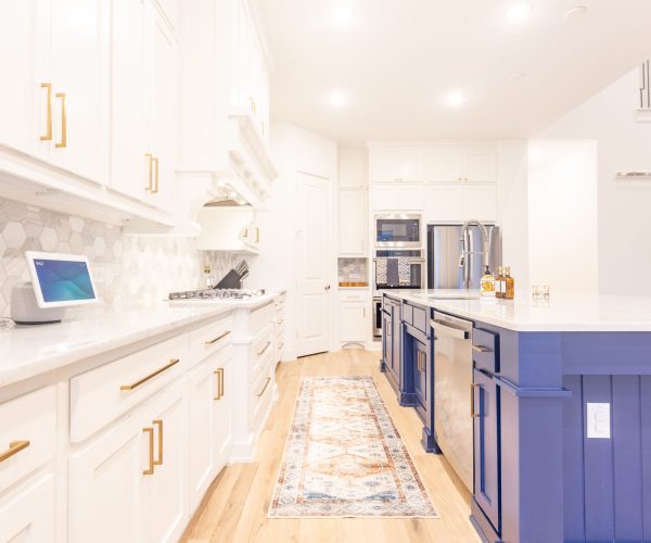 Modern kitchen featuring white cabinetry with gold hardware, a blue kitchen island, and a stylish rug, showcasing a sleek design ideal for remodeling services in Coppell, TX.