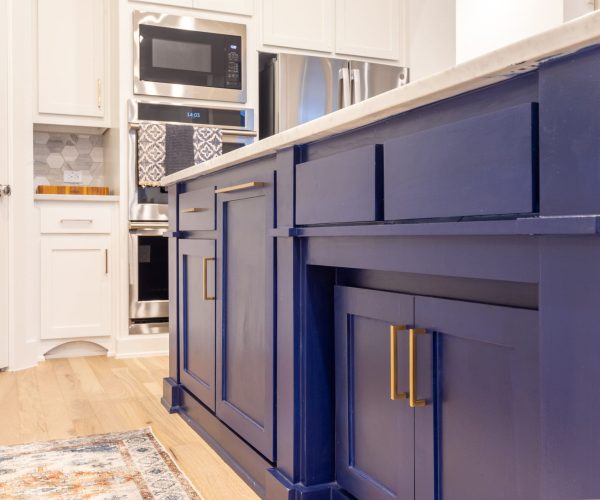 Blue kitchen island cabinetry with gold handles, stainless steel appliances in the background, and a light wood floor, showcasing high-quality craftsmanship for bathroom remodeling in Southlake, TX.