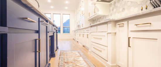 Modern kitchen interior featuring blue and white cabinetry, hardwood flooring, and bright natural light from large windows, highlighting design elements relevant to kitchen remodeling.