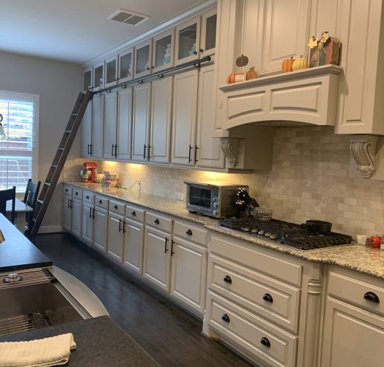 Modern kitchen with light gray cabinets, granite countertops, under-cabinet lighting, and a gas stove, featuring a ladder for access to upper cabinets, emphasizing a contemporary and functional design ideal for open layouts.