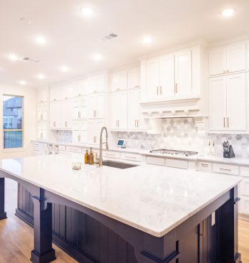 Modern kitchen featuring a large white marble countertop with a central sink, elegant cabinetry, and stylish lighting, showcasing a blend of functionality and design for home remodeling.