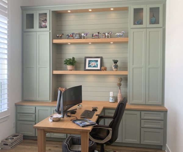 Custom home office cabinetry with green finish, open shelving displaying decorative items, and a wooden desk with a computer setup, emphasizing tailored storage solutions for functional workspace.