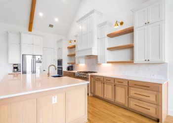 Modern kitchen design featuring custom cabinetry, spacious island with sink, stainless steel appliances, and elegant lighting, showcasing The Perfect Cabinet's craftsmanship and style for kitchen remodeling.