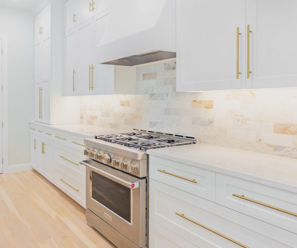 Modern kitchen with white cabinetry, gold hardware, stainless steel range, and marble backsplash, showcasing expert remodeling by The Perfect Cabinet.