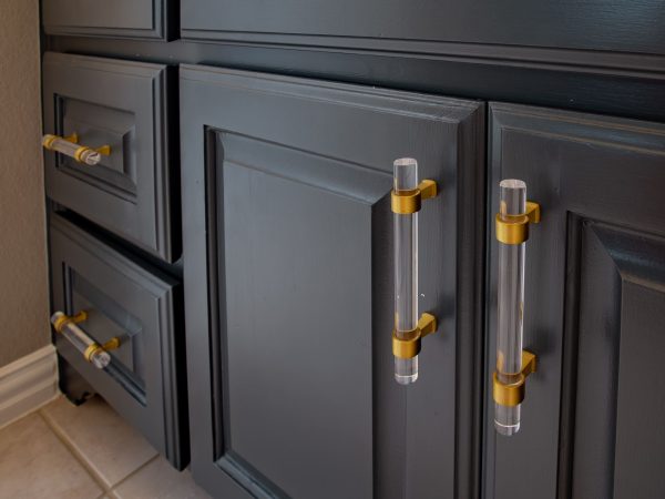 Modern kitchen cabinetry with sleek black finish, featuring gold and clear acrylic handles, highlighting custom design and craftsmanship for kitchen remodels.