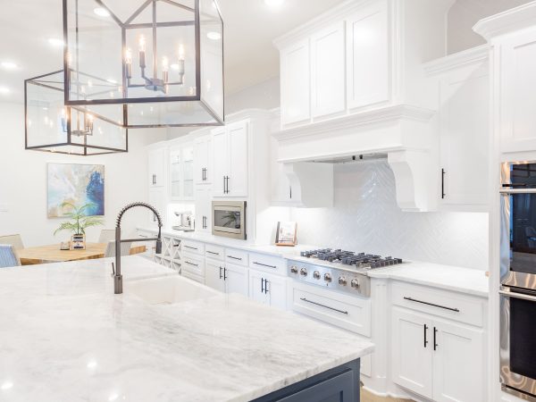 Modern kitchen featuring white cabinetry, marble countertops, and stainless steel appliances, with a large island and stylish pendant lighting, showcasing a blend of beauty and functionality for kitchen remodeling inspiration.