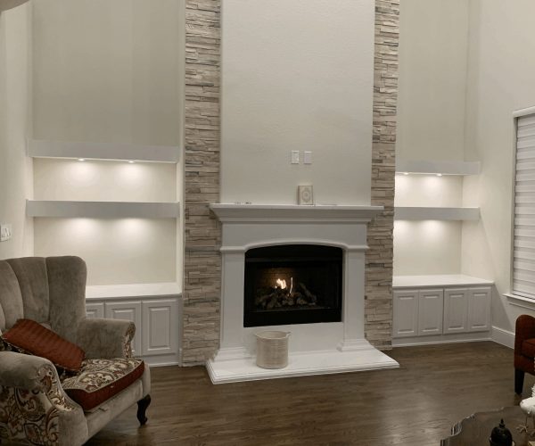 Modern living room featuring a stone fireplace with built-in shelves, elegant armchair, and warm wood flooring, showcasing custom cabinetry and stylish design elements.