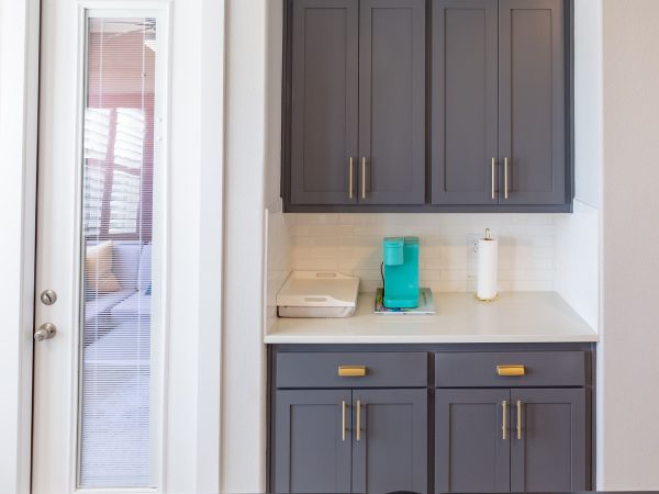 Custom gray kitchen cabinets with gold hardware, countertop with teal water pitcher and paper towel holder, adjacent to a glass door, showcasing organization and modern design in home renovation.